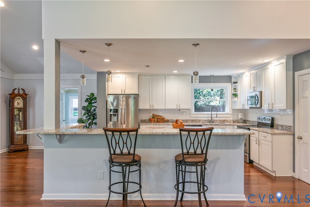Kitchen featuring white cabinetry, stainless steel appliances, granite countertops, a tile backsplash, and wood-finish flooring
