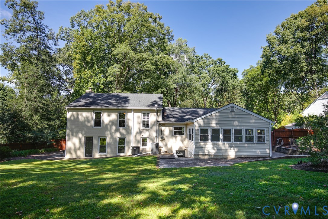 Expansive rear yard with a manicured lawn, established landscaping, and a patio area