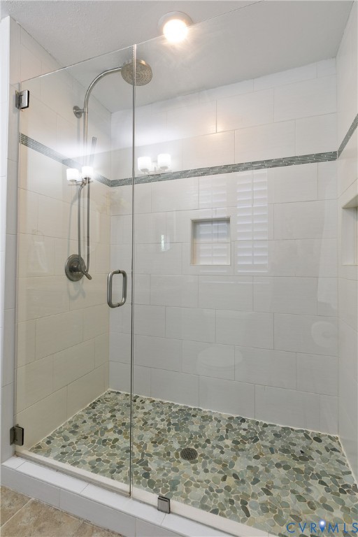 Glass-enclosed shower with pebble-tile flooring, white subway tile walls, and a recessed niche