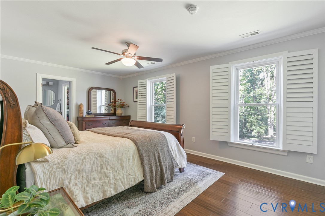 Wood-finish flooring, ceiling fan with integrated lighting, crown molding, white plantation shutters, and a doorway opening to an additional room