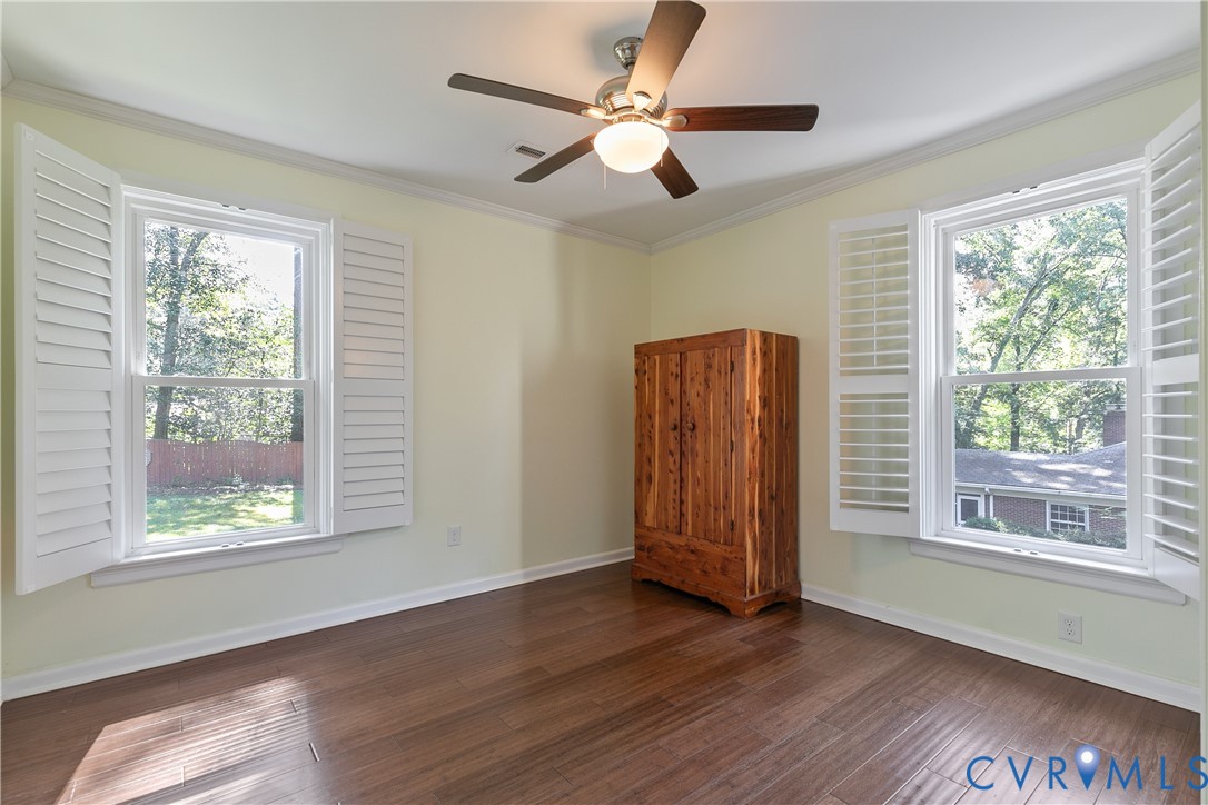 Wood-finish flooring, crown molding, ceiling fan with integrated lighting, and white plantation shutters on two windows