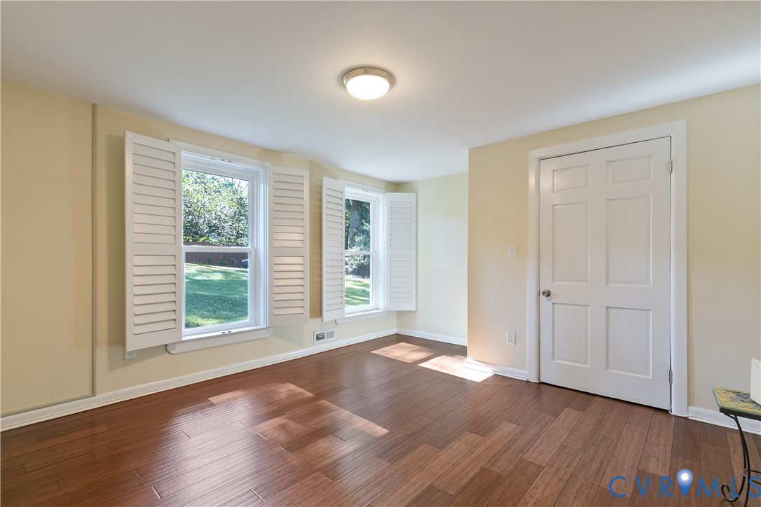 Hardwood-style flooring, multiple windows with white shutters, ceiling-mounted light fixture, and a six-panel interior door