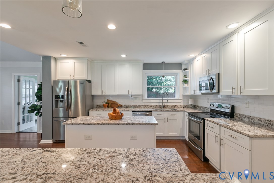 Kitchen featuring white cabinetry, granite countertops, stainless steel appliances, a center island, and wood-finish flooring