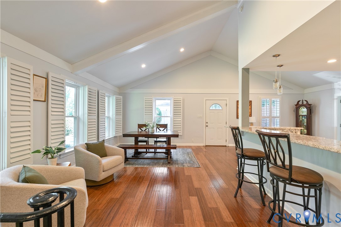 Vaulted ceilings with exposed beams, wood-finish flooring, plantation shutters, and a kitchen pass-through with a granite countertop