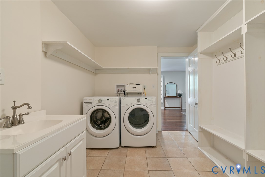Tile flooring, built-in shelving, integrated coat hooks, utility sink with storage vanity, and overhead shelving