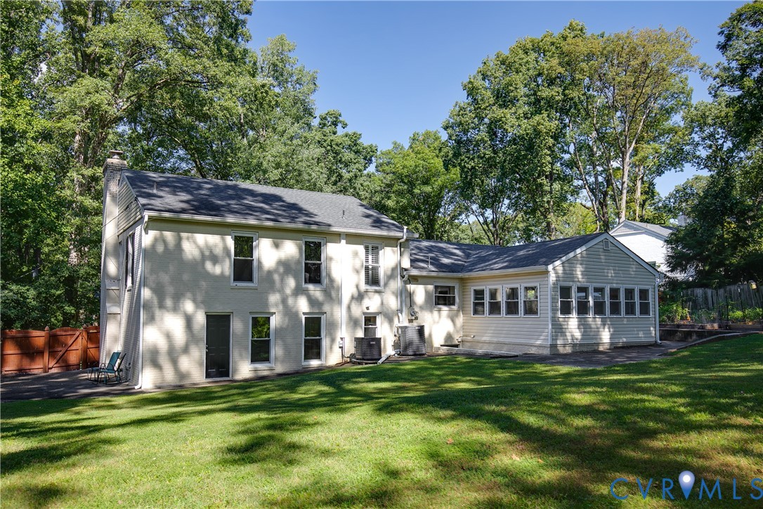 Expansive green lawn with mature trees and a multi-level home featuring an extended sunroom with multiple windows