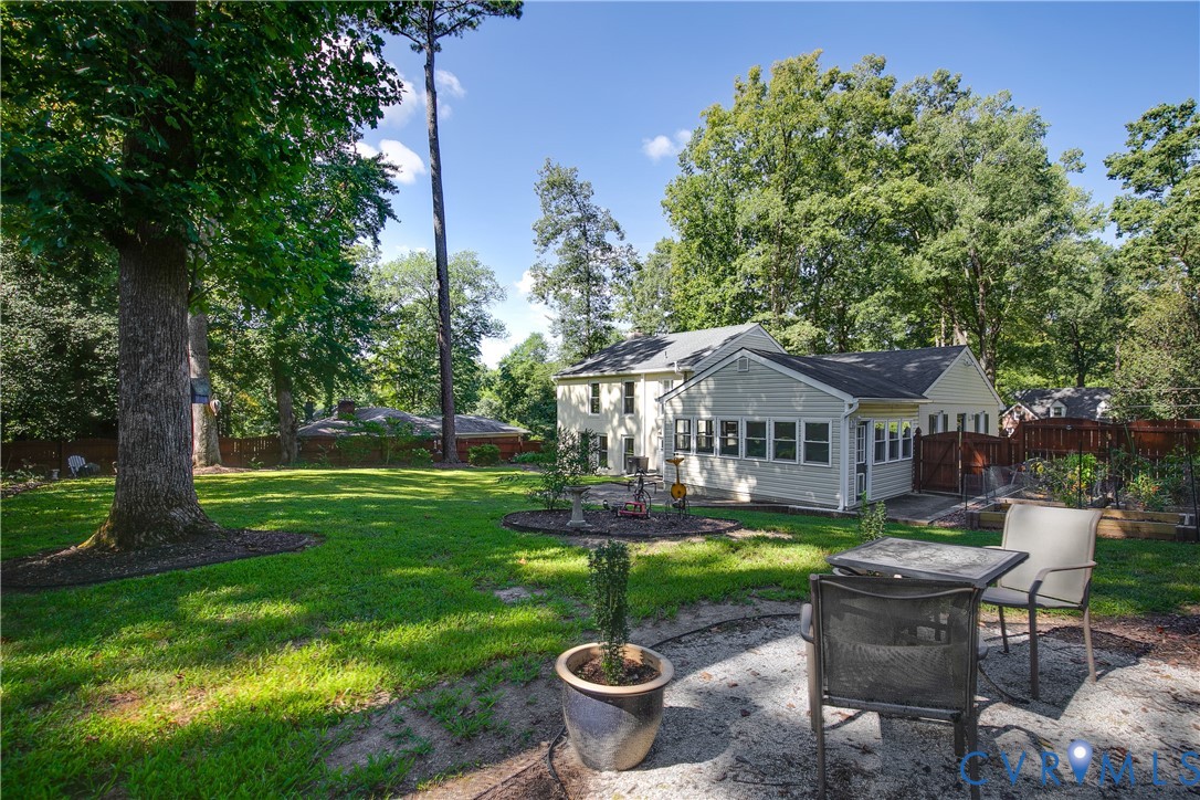 Expansive backyard featuring a manicured lawn, mature trees, and a stone patio