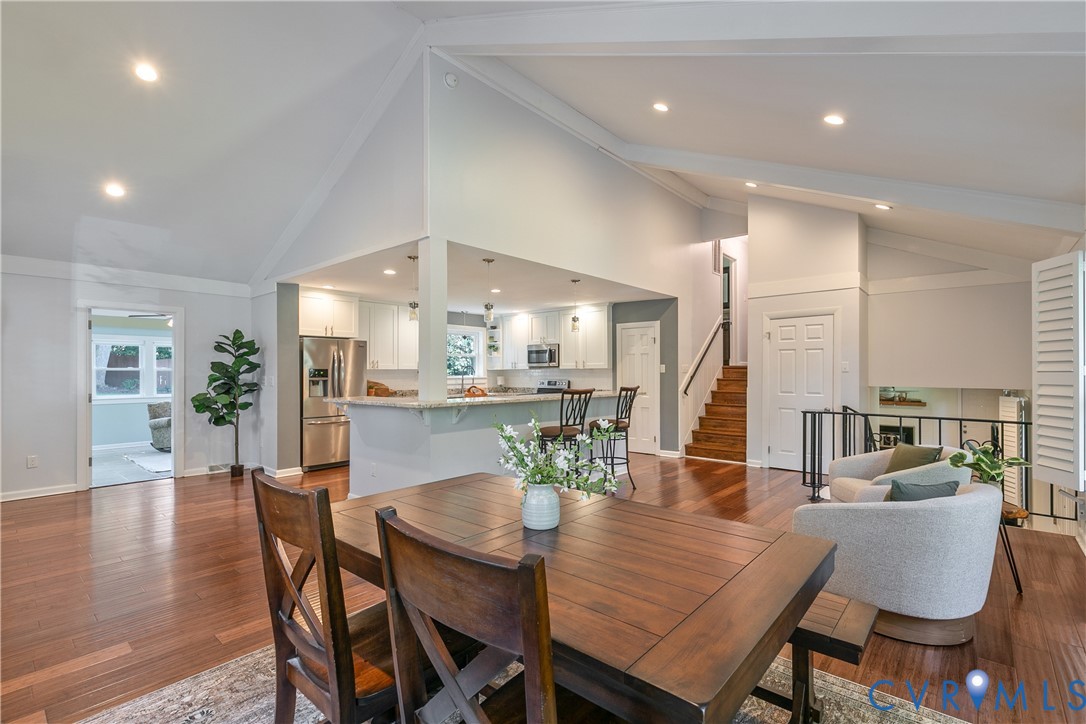 Vaulted ceilings with exposed beams, recessed lighting, wood-finish flooring, white cabinetry, and stainless steel appliances