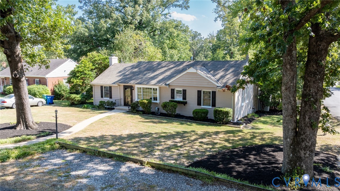 Single-story exterior with a gabled roofline, front lawn, mature trees, and a curved sidewalk