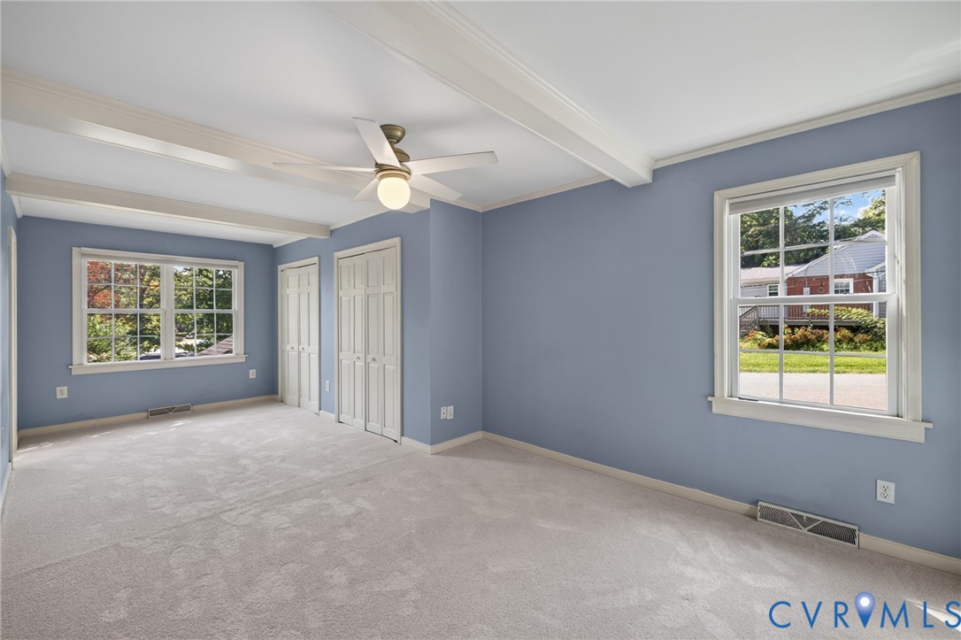 Exposed ceiling beams, dual windows, ceiling fan, and light gray carpeted flooring