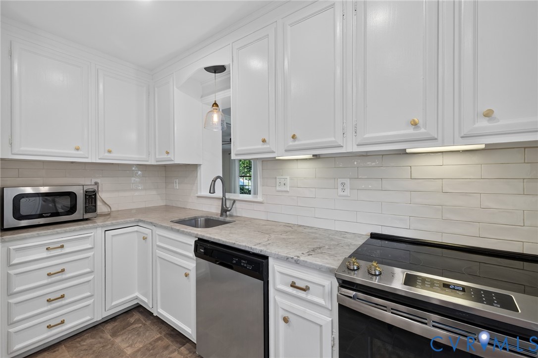 White cabinetry with brass hardware, light-toned countertops, white subway tile backsplash, stainless steel appliances, and a stainless steel sink