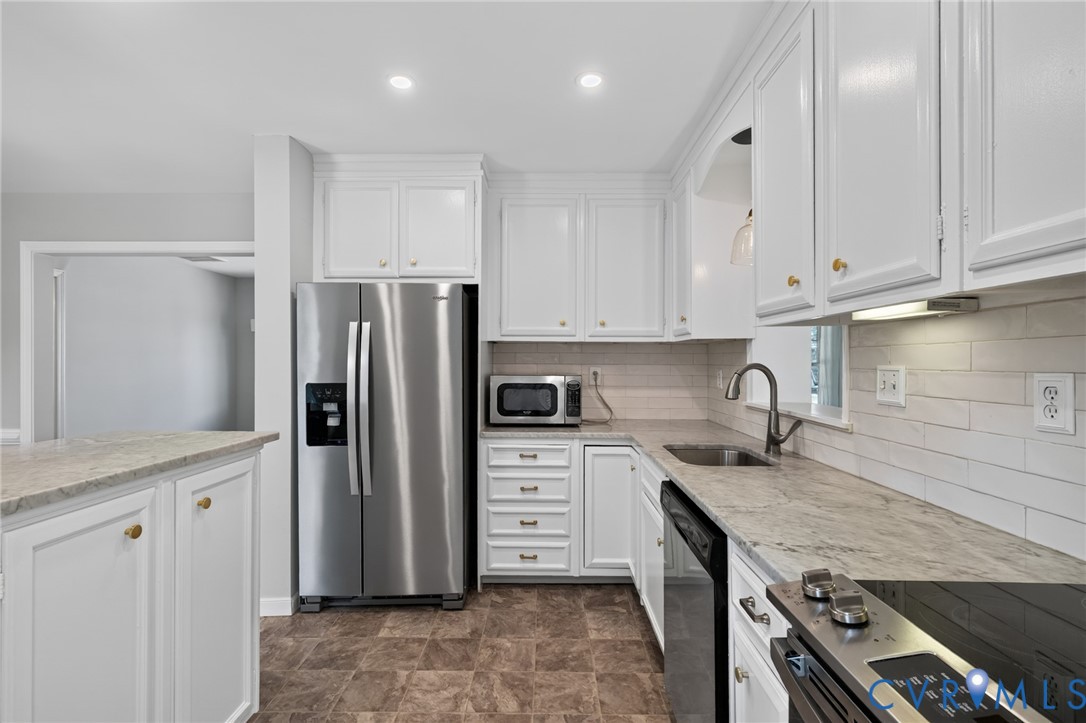 White shaker-style cabinetry with gold-tone hardware, stainless steel appliances, light-toned countertop, and a subway tile backsplash