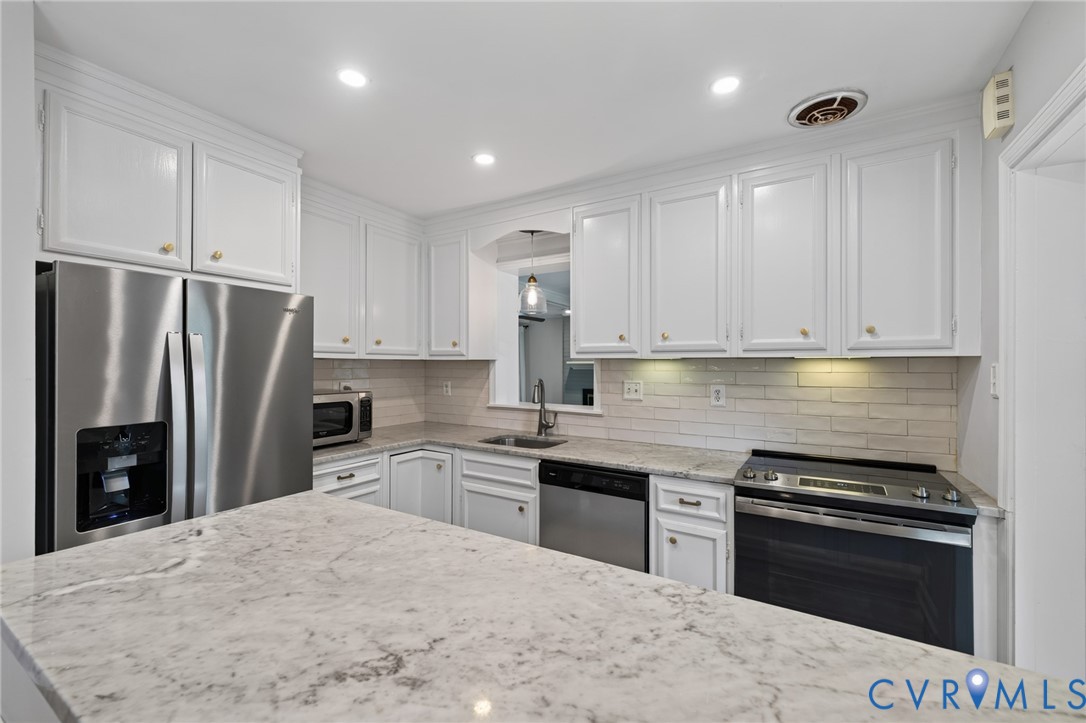 Kitchen featuring white cabinetry with gold-toned hardware, light-toned countertops, a stainless steel side-by-side refrigerator, a stainless steel dishwasher, and an electric range