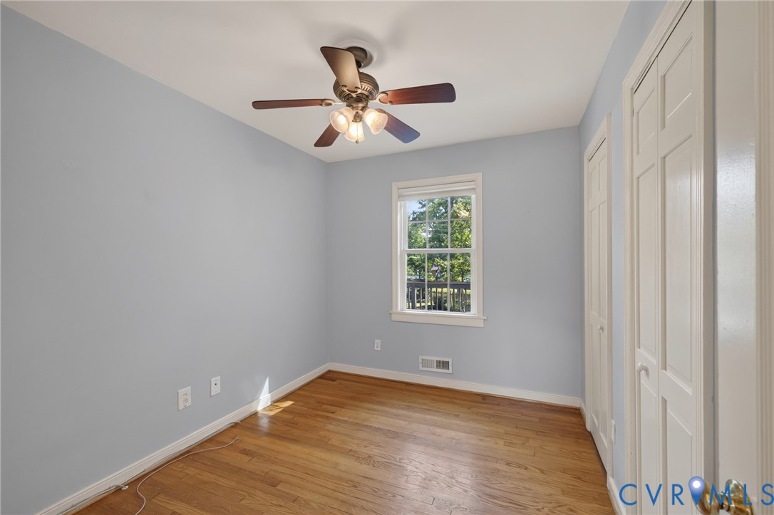 Hardwood flooring, painted walls, single window, louvered closet doors, and a ceiling fan with integrated lighting