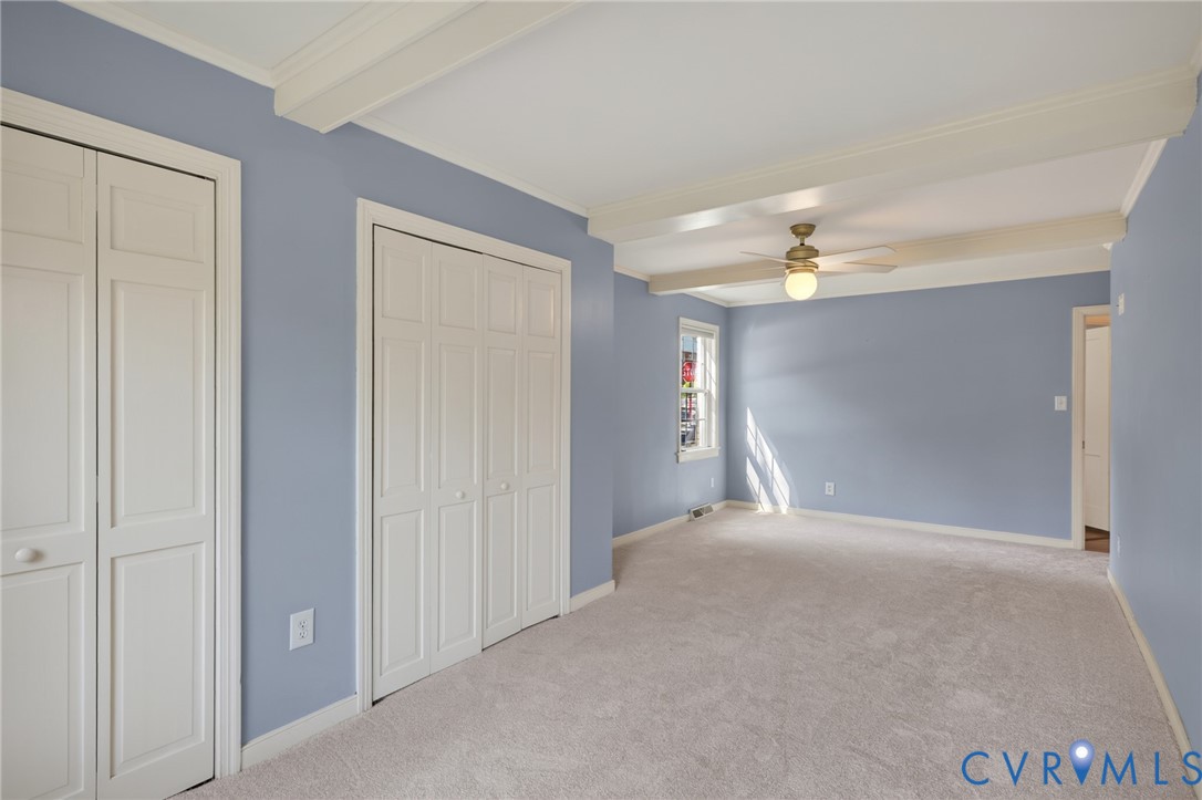 Beamed ceiling with an integrated ceiling fan, light-toned carpeting, and a window with natural light