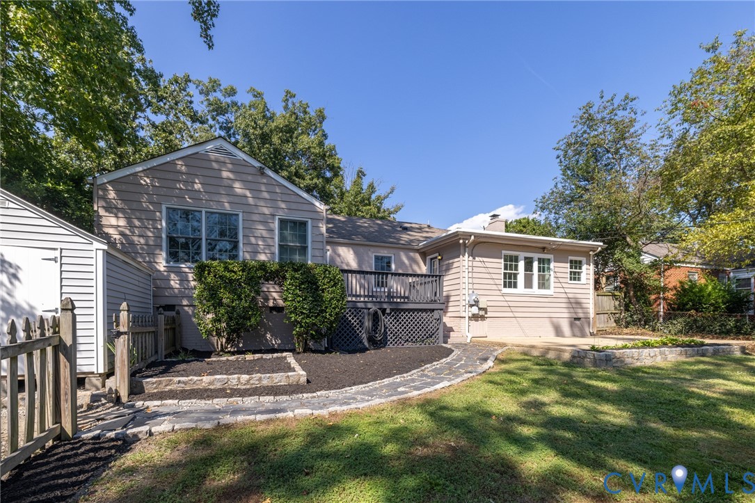 Exterior siding with multiple windows, elevated rear deck, paved walkway, and a detached storage shed