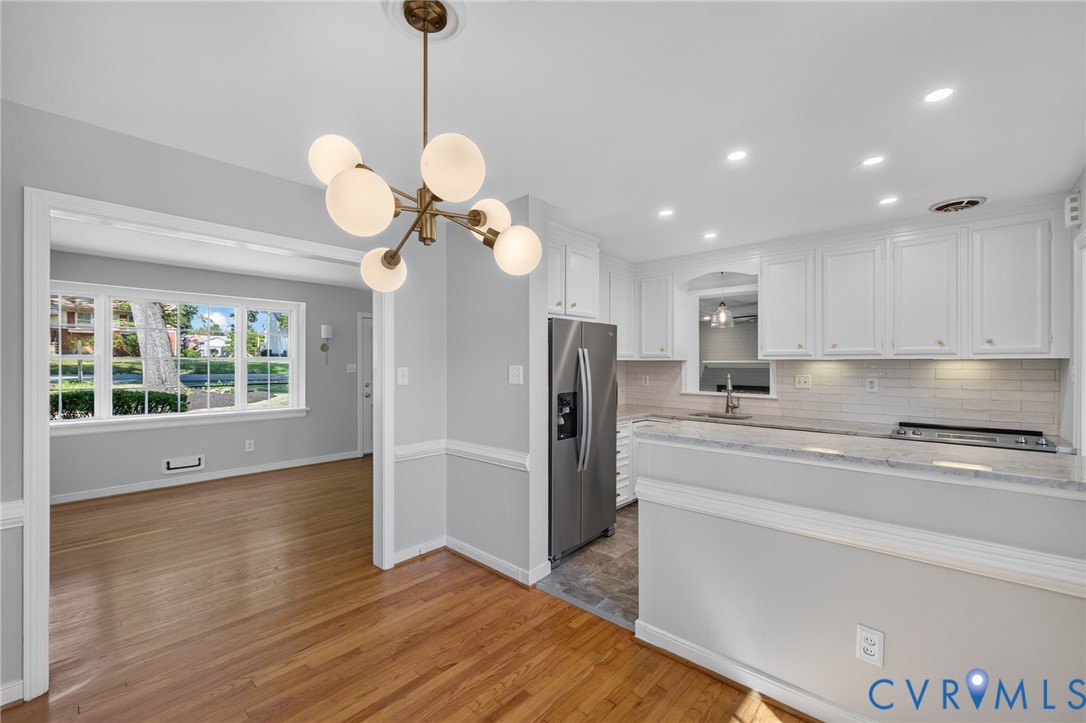 Modern chandelier, wood-finish flooring, white cabinetry, integrated stainless steel appliances, and recessed lighting