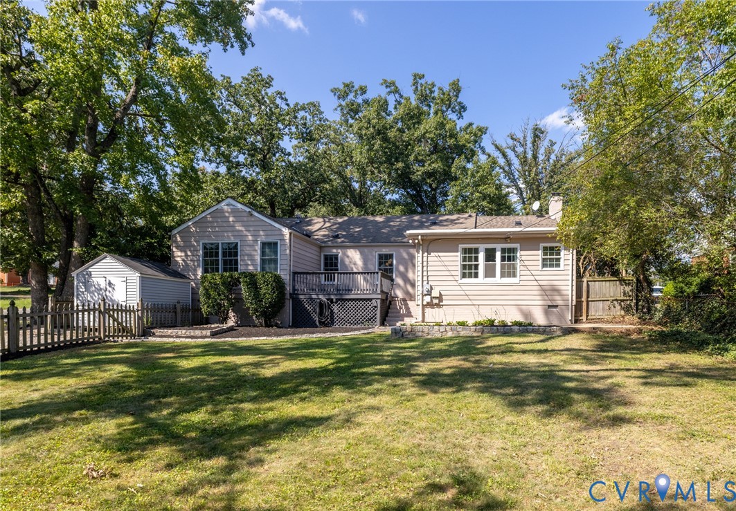 Expansive backyard featuring a manicured lawn, picket fencing, mature trees, and a multi-level deck