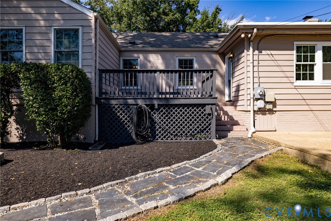 Elevated wood deck with lattice skirting, stone paver pathway, and manicured landscaping