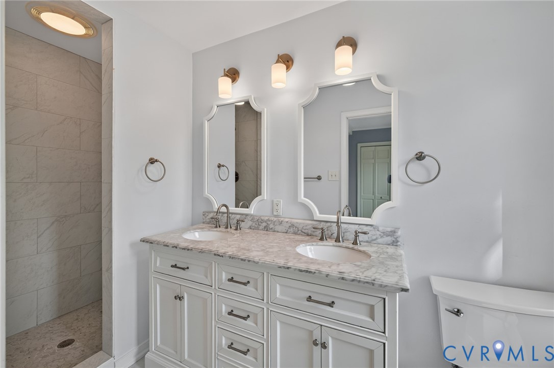 Dual vanity with white cabinetry, stone countertop, two undermount sinks, and decorative mirrors