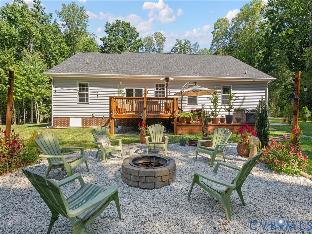 Rear exterior featuring a wood deck, stone fire pit, and gravel patio area