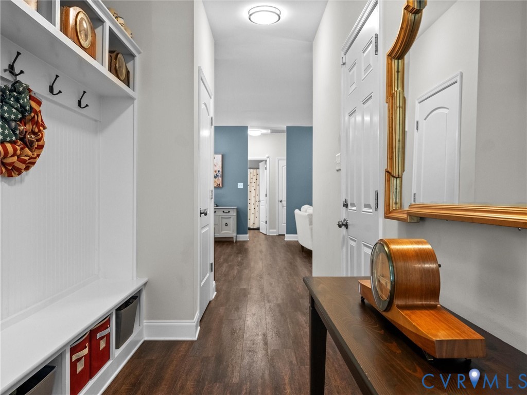 Hallway featuring wood-finish flooring, a built-in white mudroom bench with storage cubbies, and a decorative wall mirror