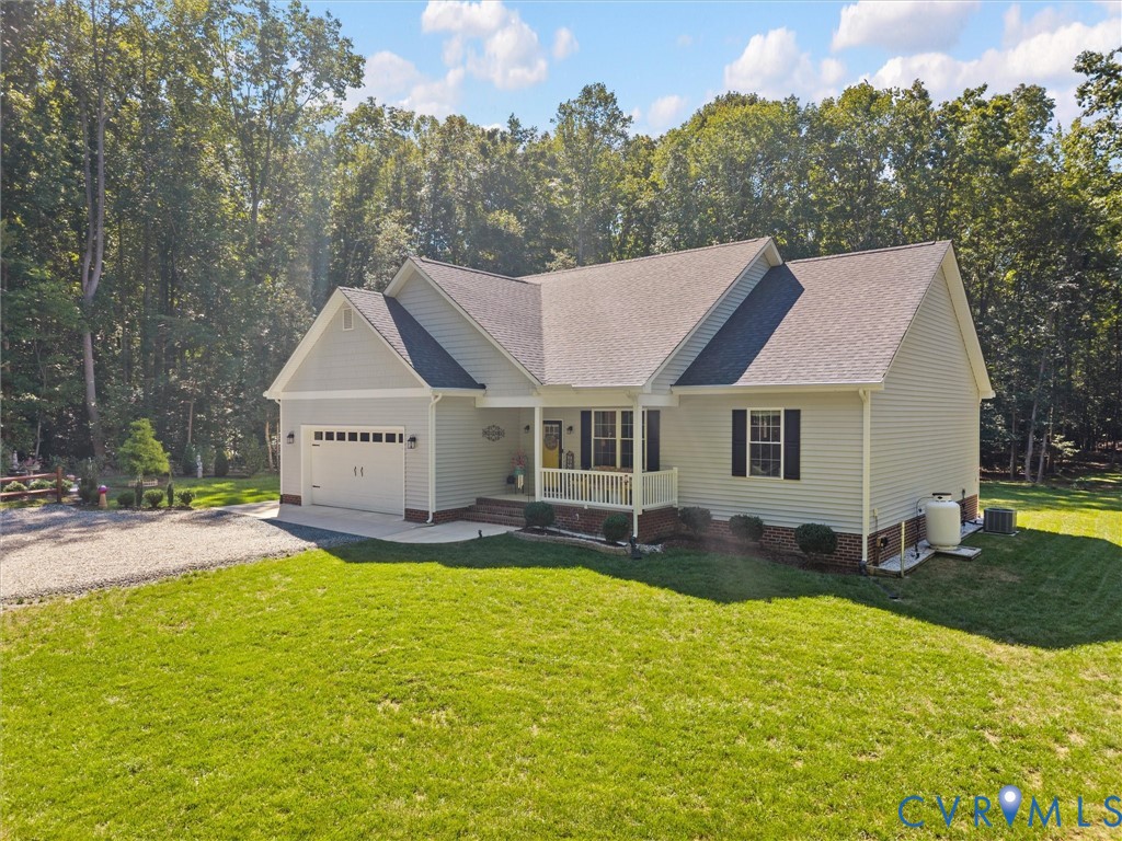 Light-colored siding exterior, attached two-car garage, covered front porch, gravel driveway, and surrounding green lawn