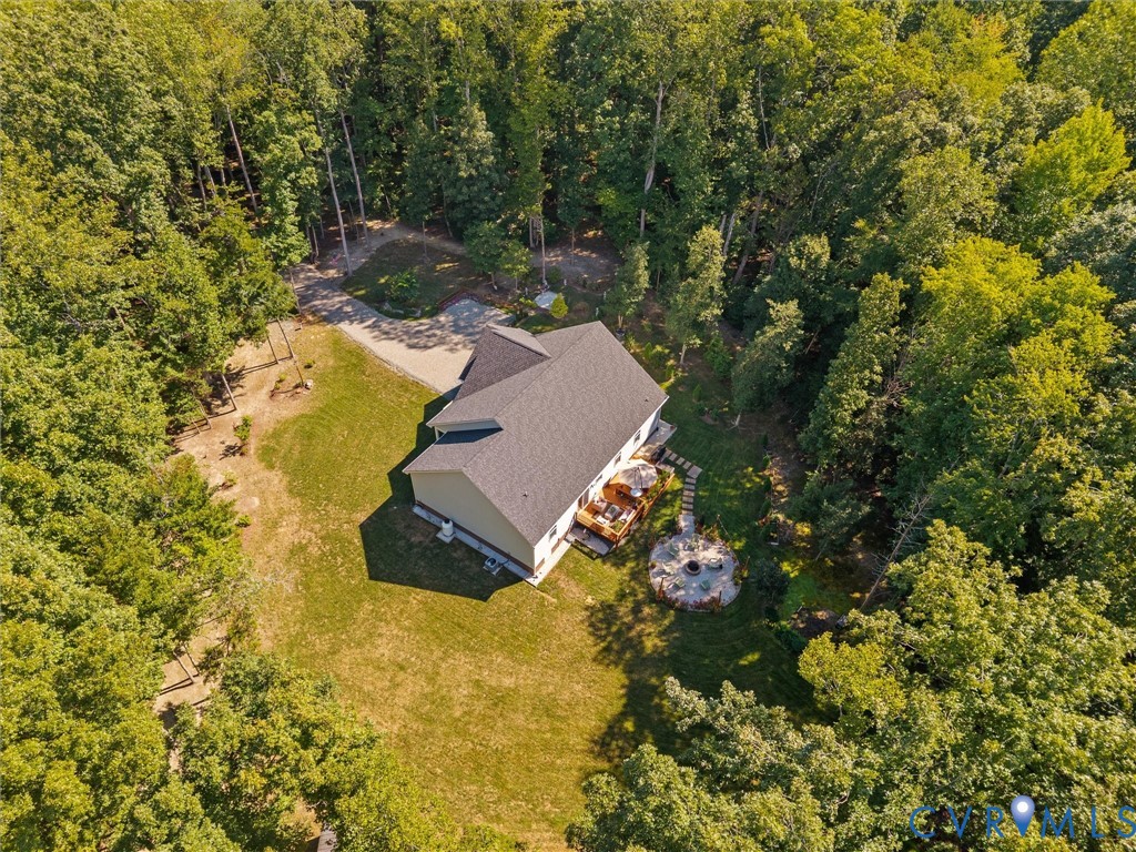 Expansive wooded property featuring a residential structure with a shingle roof, a gravel driveway, a wood deck, a stone patio, and a built-in fire pit