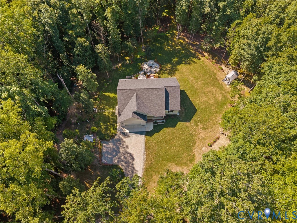 Wooded property featuring a multi-level residence, attached garage, and gravel driveway