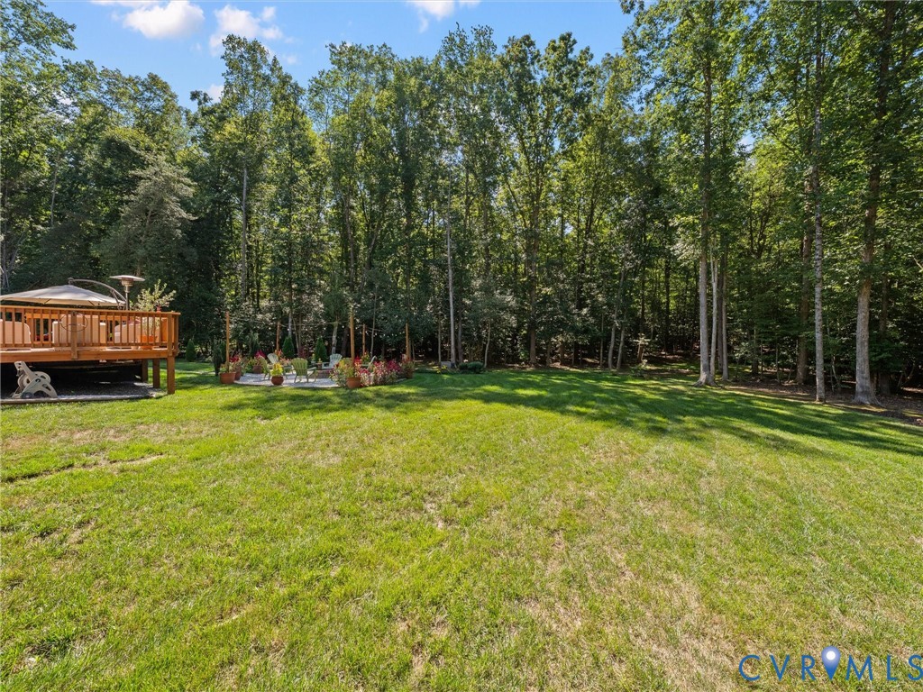 Expansive grassy lawn with a wood-finish deck featuring a built-in pergola and a stone-paver patio, all surrounded by mature trees