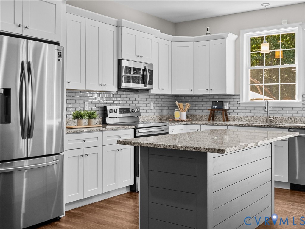 White shaker-style cabinetry, stainless steel appliances, light-toned granite countertops, a subway tile backsplash, and wood-finish flooring
