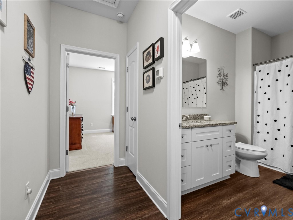 White vanity with granite countertop, wood-finish flooring, and a shower with a curtain rod