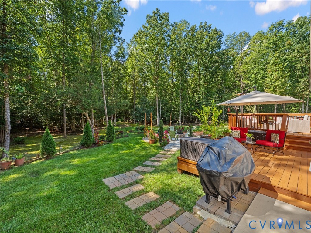 Expansive backyard featuring a manicured lawn, stone paver pathway, and a multi-level wood-finish deck