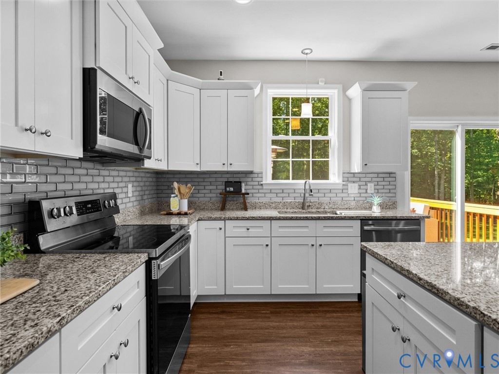 White cabinetry, granite countertops, subway tile backsplash, stainless steel appliances, and wood-finish flooring