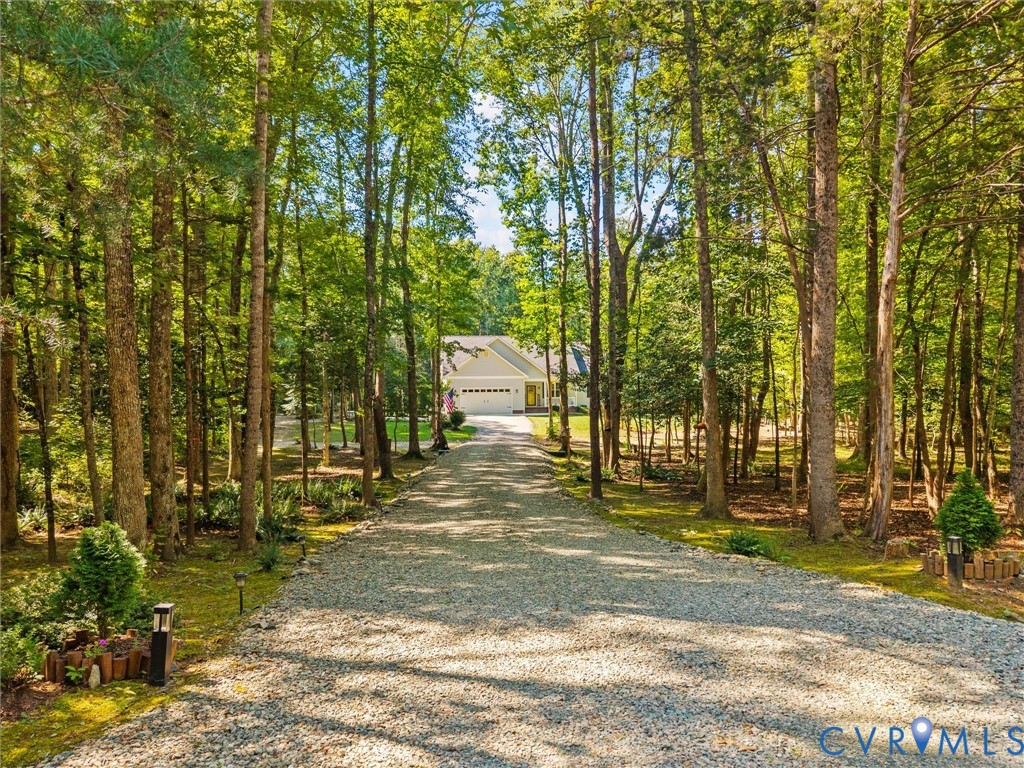 Gravel driveway leading to a single-story residence with a two-car garage, surrounded by mature trees