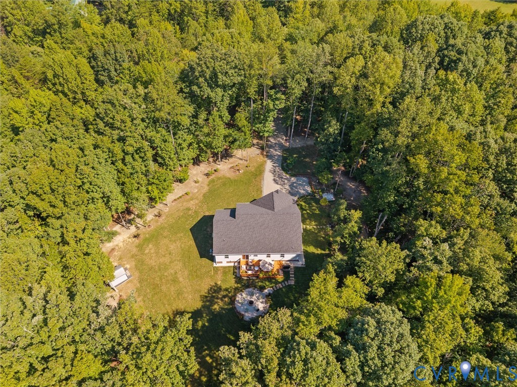 Expansive wooded surroundings with a gravel driveway, a large rear deck, a fire pit area, and a white shed
