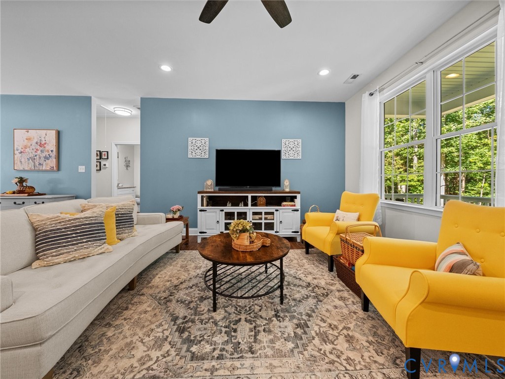 Recessed lighting, ceiling fan, white trim windows, wood-finish media console, and light blue wall finishes