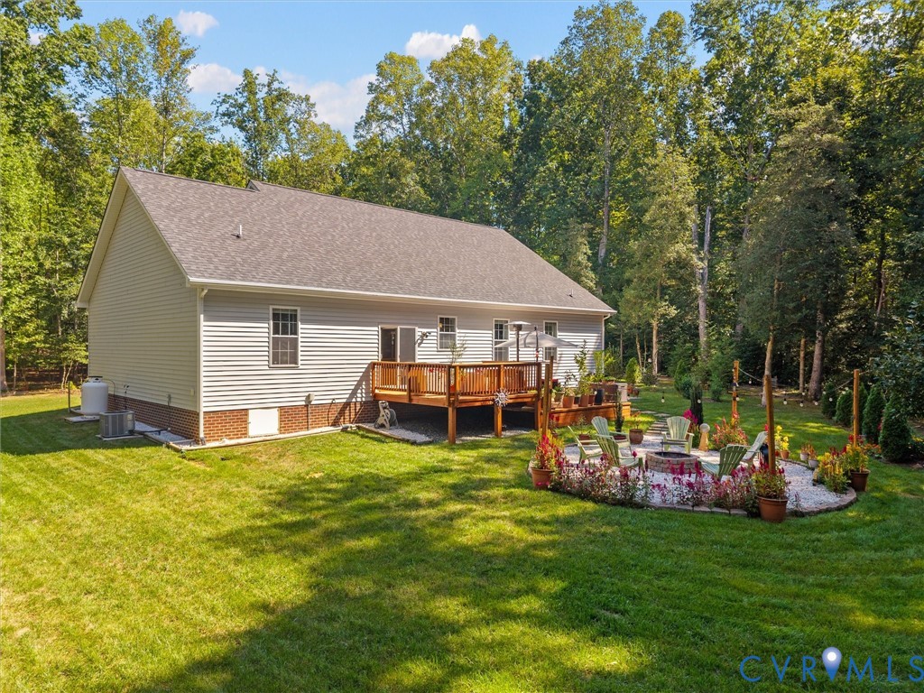 Expansive backyard featuring a manicured lawn, a multi-level wood deck, a stone fire pit area, and mature trees
