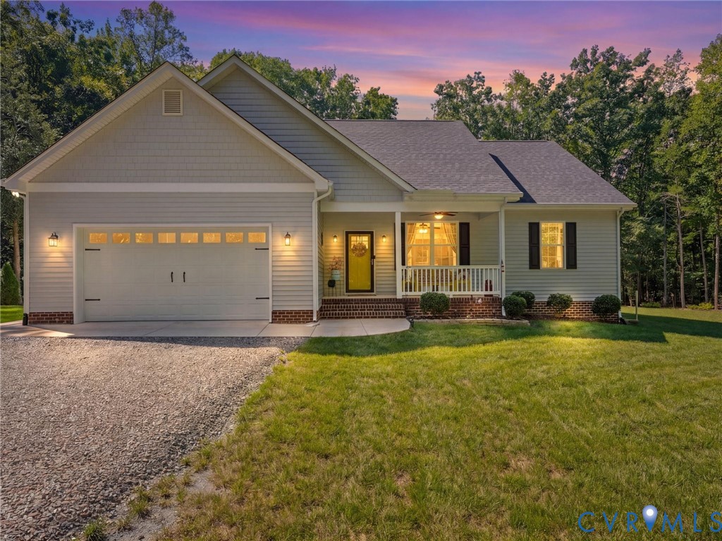 Siding exterior with brick accents, covered front porch, gravel driveway, and attached garage