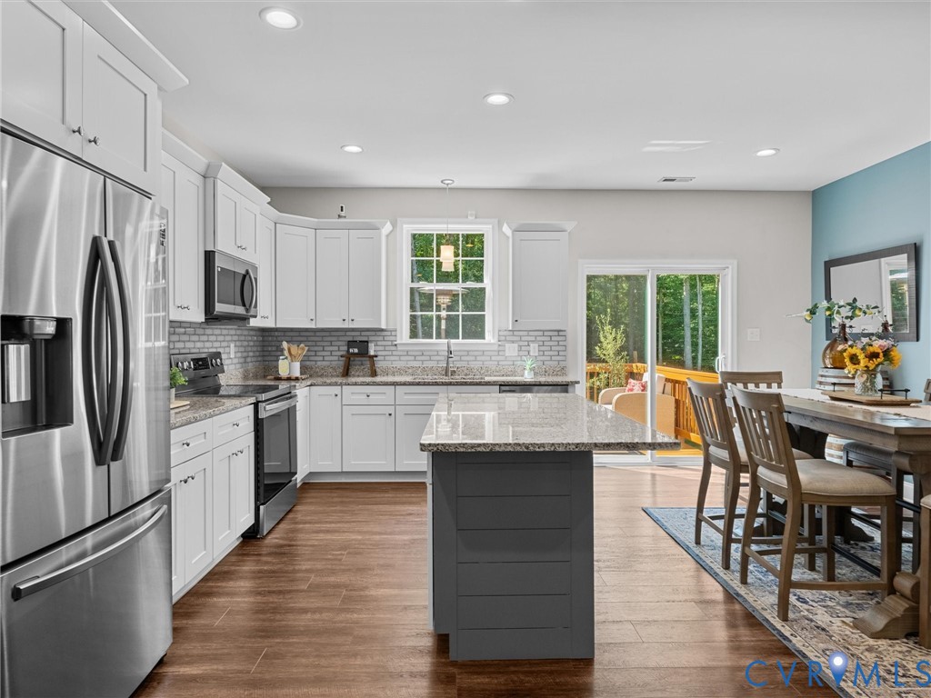Kitchen featuring white cabinetry, stainless steel appliances, a center island with countertop seating, wood-finish flooring, and a sliding glass door to exterior