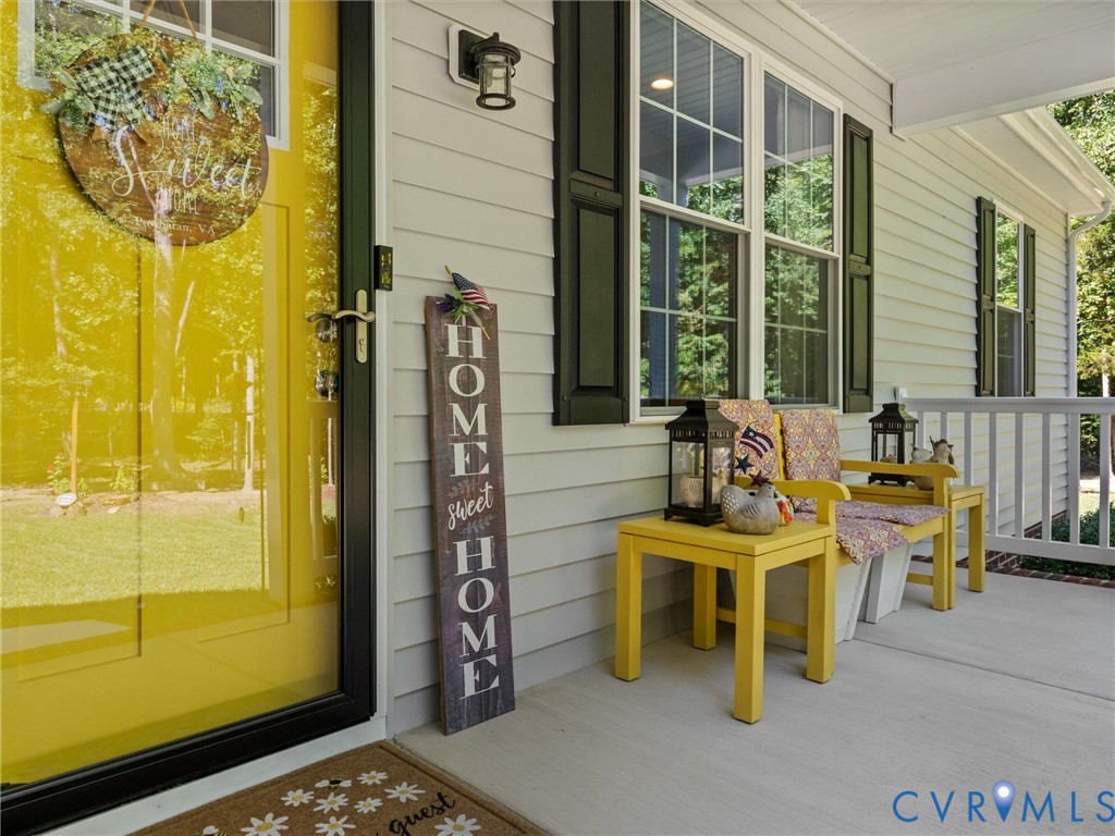 Front entrance featuring a bright yellow door, white siding, dark shutters, an exterior wall light, and a white porch railing