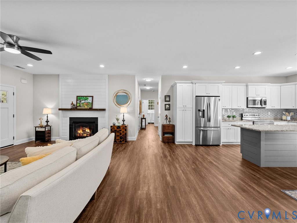 Open-concept living area featuring wood-finish flooring, a white-tiled fireplace, a ceiling fan, white cabinetry, and stainless steel appliances