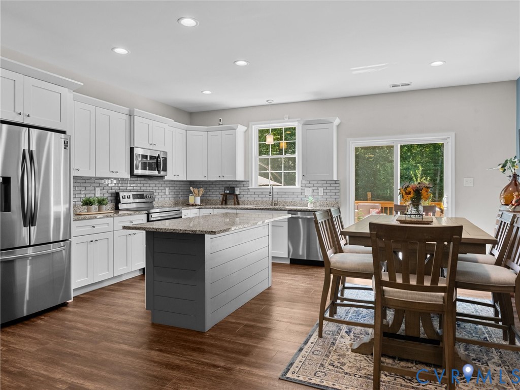 Kitchen featuring white cabinetry, stainless steel appliances, a center island with a stone countertop, wood-finish flooring, and a sliding glass door