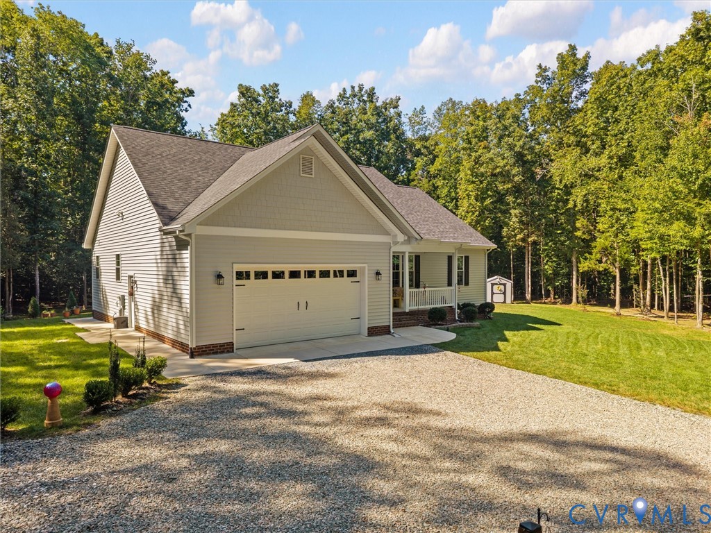 Light-toned siding exterior with a dark shingle roof, attached two-car garage, covered porch, and gravel driveway