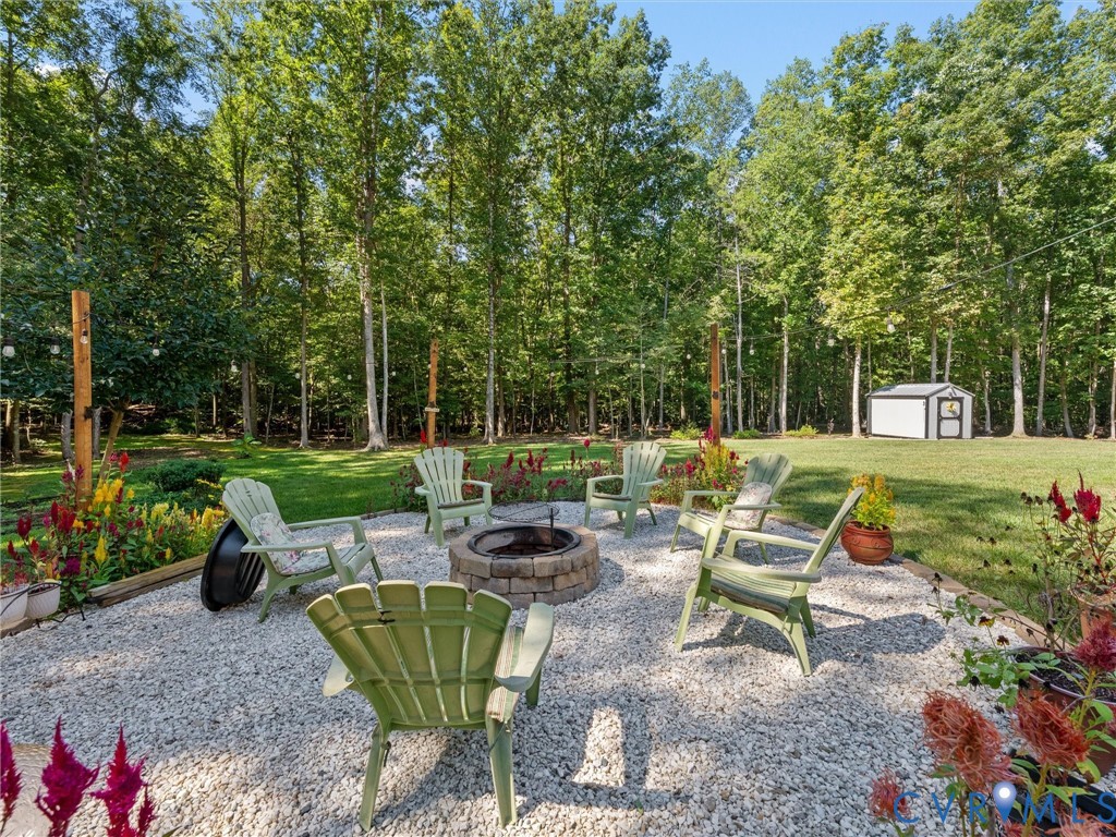 Gravel patio with a built-in fire pit, surrounded by lush green lawn and mature trees