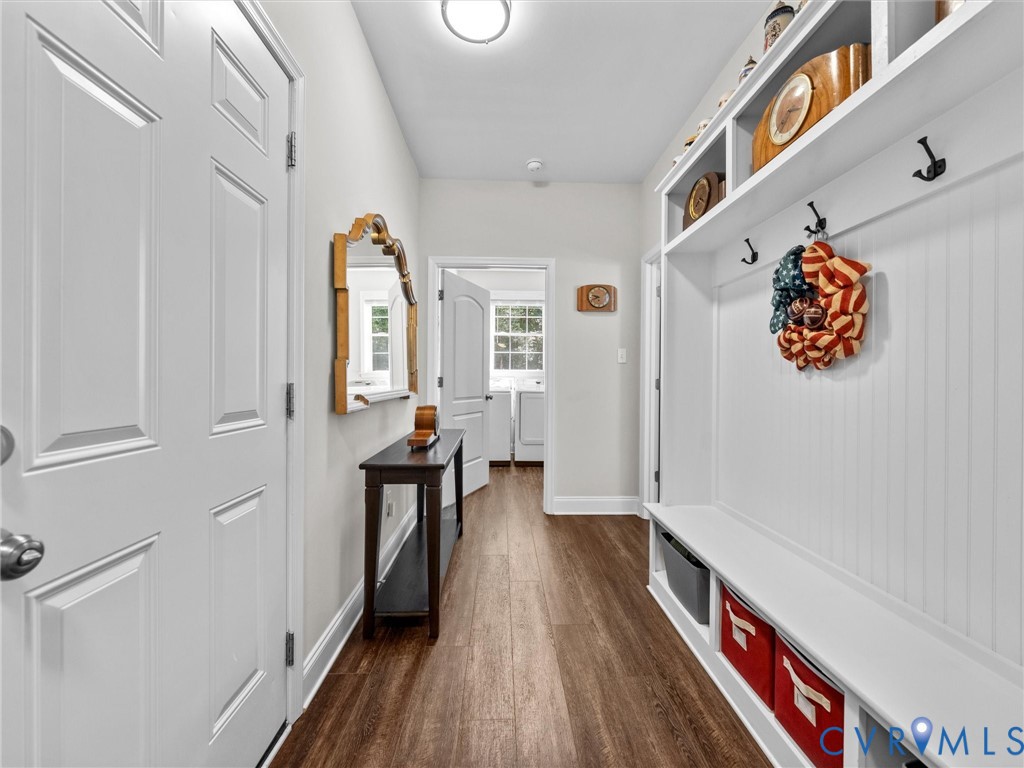 Entryway featuring white paneled doors, built-in mudroom seating with storage, upper shelving, and wood-finish flooring