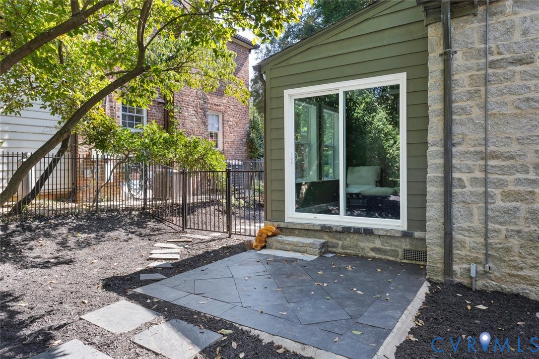 Stone patio with irregular-shaped pavers, featuring a white-framed sliding glass door and stone foundation