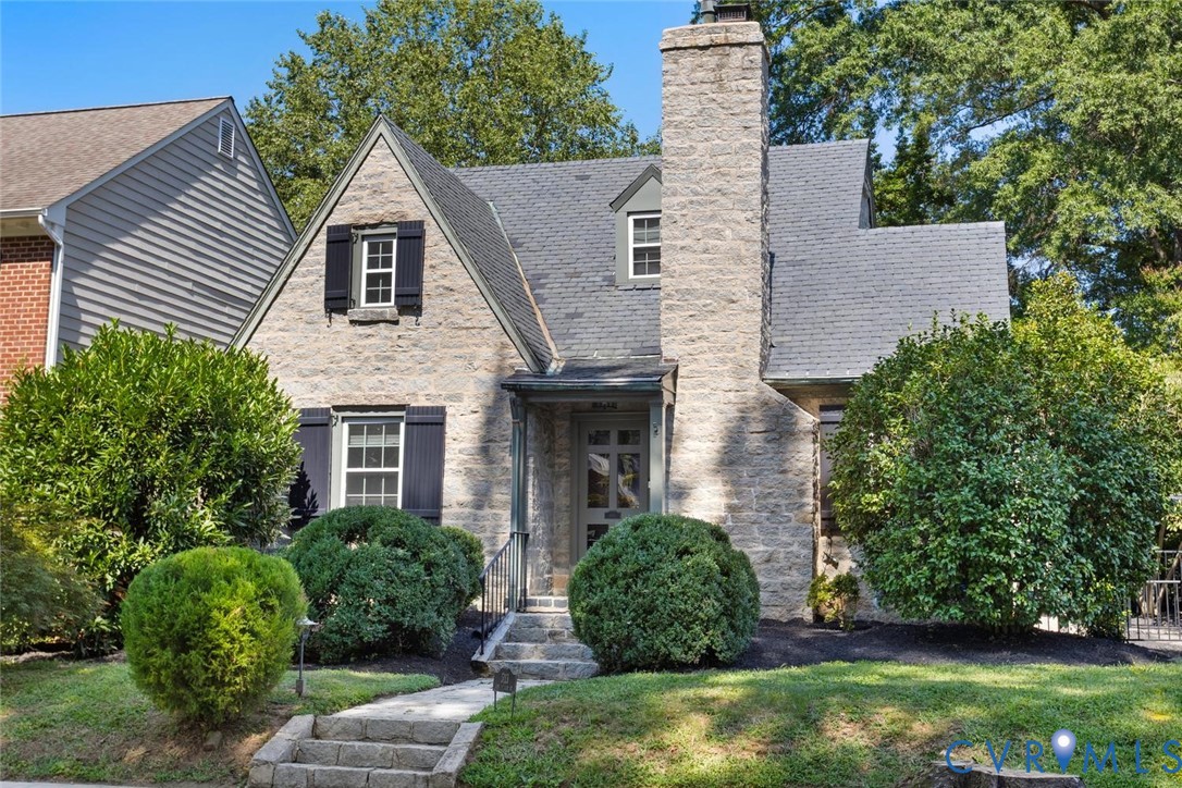 Stone exterior with a prominent stone chimney, dark shingle roof, and shuttered windows