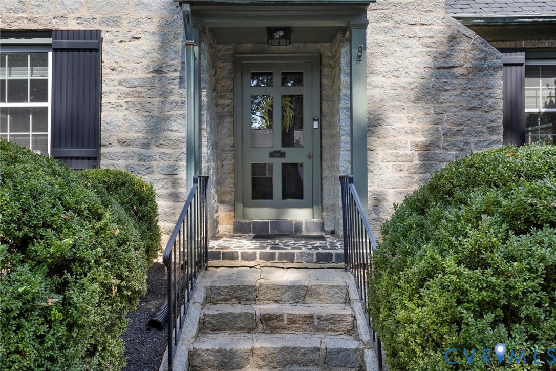 Stone facade with a paneled entry door, black wrought iron railings, and stone steps leading to the entrance