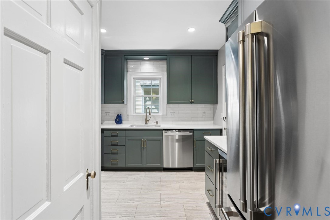 Kitchen with dark green cabinetry, white countertops, tile backsplash, and stainless steel appliances